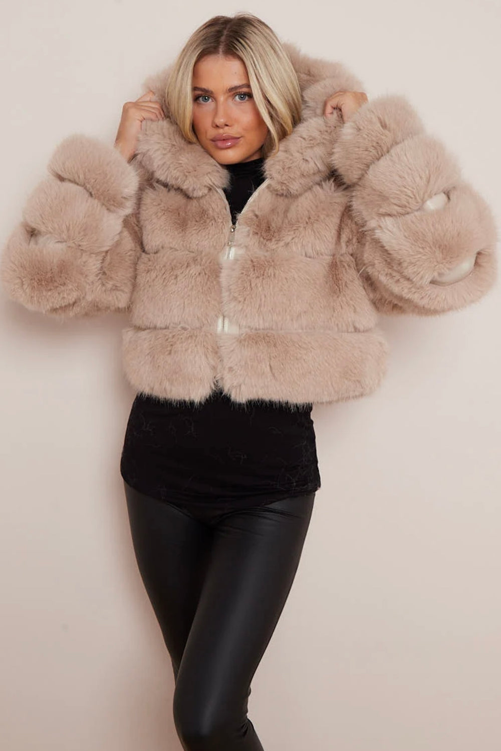A model wearing a beige cropped faux fur hood coat with a snuggly hood, paired with black leggings.