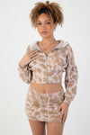 A woman modeling a matching beige and white tie-dye two-piece set consisting of a cropped zip-up hoodie with a hood and a matching mini skirt, set against a plain white background.