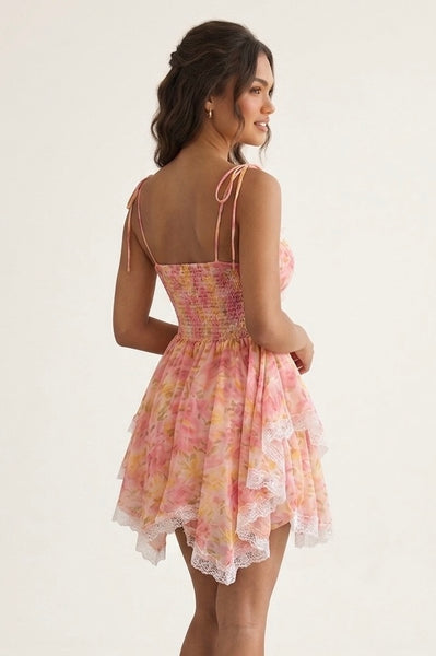 A woman modeling a short pink and yellow tie-dye dress with lace trim and thin shoulder ties, shown from the back against a plain light background.
