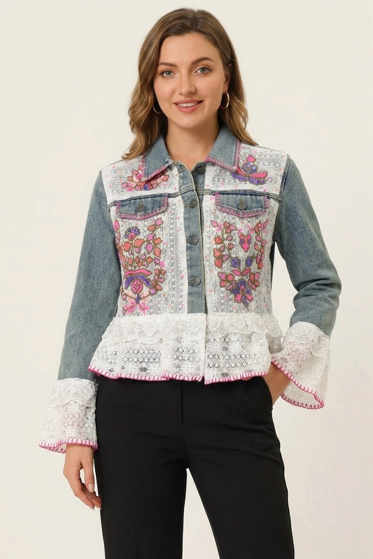 A woman modeling a denim jacket with intricate floral embroidery on the front, white lace applique on the collar, hem, and cuffs, and black pants, set against a plain light background.