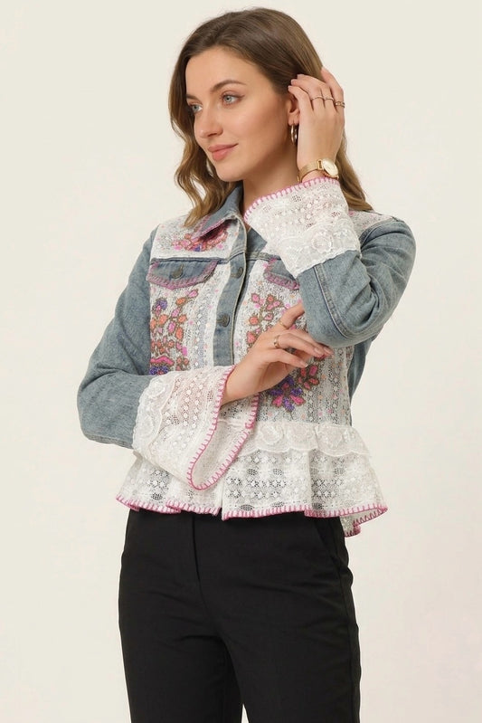 A woman modeling a cropped denim jacket with white lace trim and colorful floral embroidery on the front, paired with black pants against a plain light background.