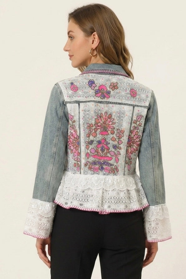 A woman shown from the back wearing a light-wash denim jacket with extensive pink, purple, and green floral embroidery across the back and white lace trim at the hem and cuffs, paired with black pants.
