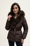 A woman wearing a dark brown puffer jacket with a large brown fur-trimmed collar and a matching belt, photographed against a plain light background.