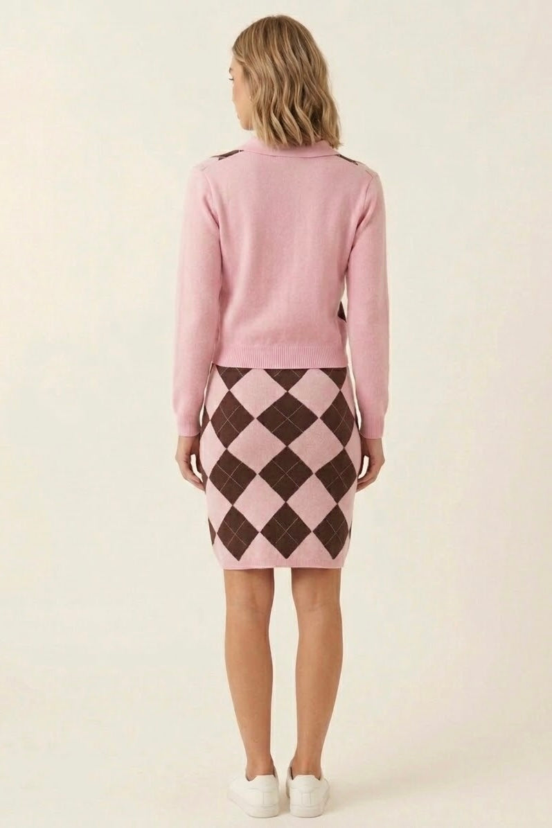 A woman shown from the back wearing a light pink knit cardigan and a pink and dark brown argyle skirt, paired with white sneakers, against a plain off-white background.