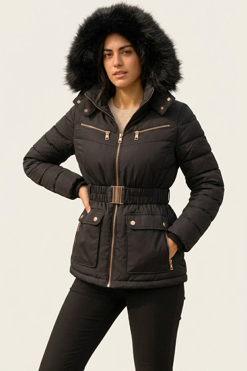 A woman modeling a black hooded puffer jacket with a black faux-fur trimmed hood, gold-tone zipper and button details, and a matching black belt, against a plain light background.