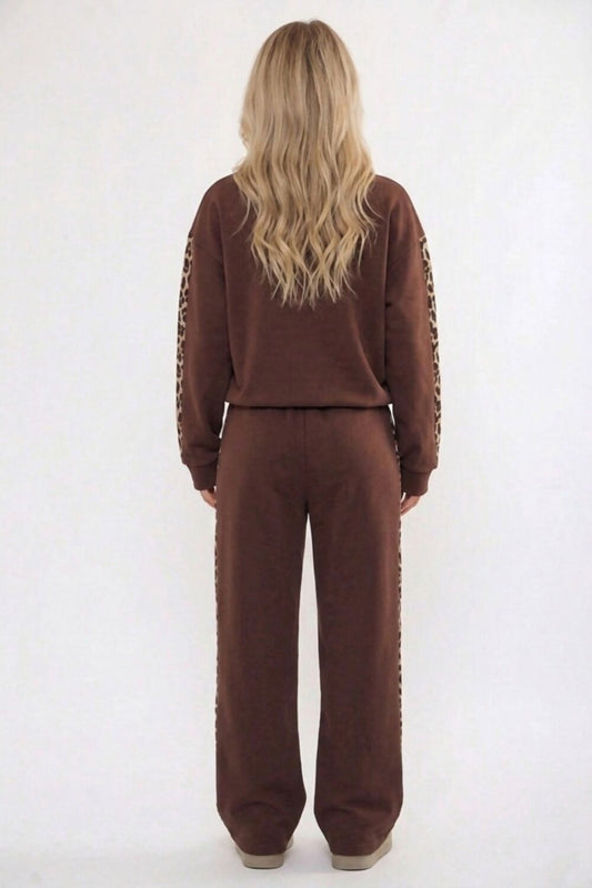 A woman viewed from behind wearing a brown two-piece lounge set with leopard-print sleeve and side details, against a plain white studio background.