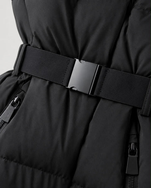 Close-up of a black puffer jacket with a wide black belt and a matte black metal buckle, showing quilted stitching and zippered pockets.