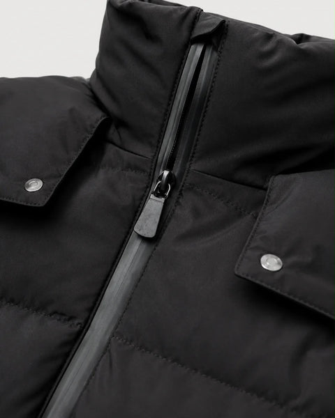 Close-up of a black puffer jacket showing the front zipper, high collar, and flap pockets with silver snap buttons.
