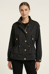 A woman modeling a black peplum-style utility jacket with gold-tone buttons and a high collar, set against a plain light background.