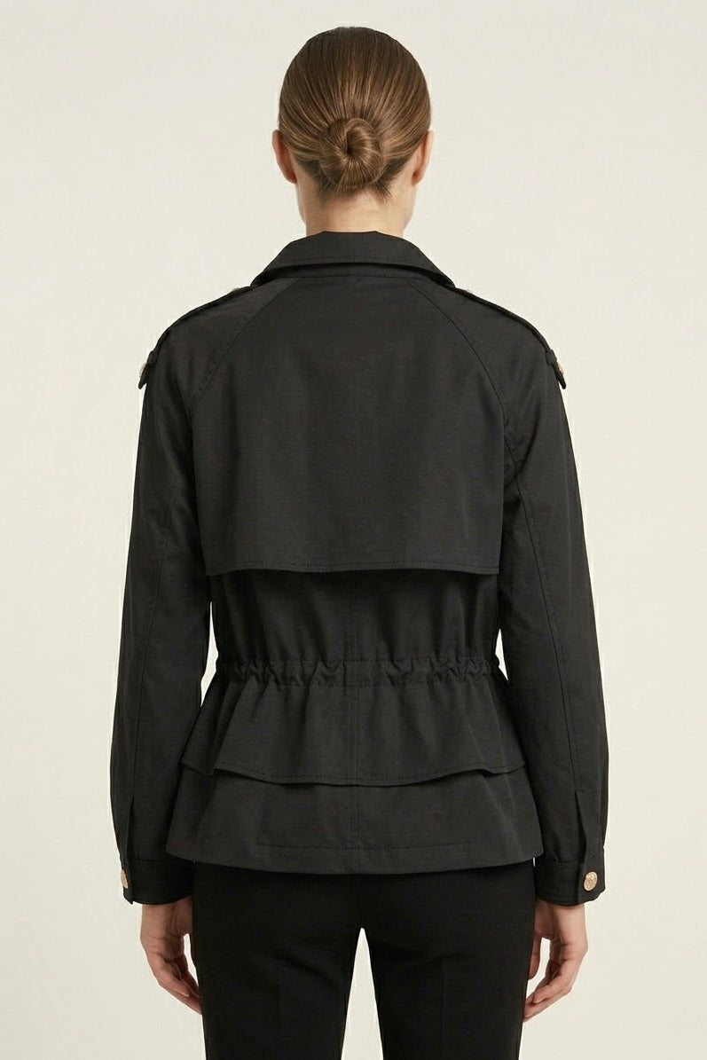 A woman viewed from the back wearing a black peplum-style jacket with shoulder epaulets and a gathered waist, paired with black pants against a plain light background.
